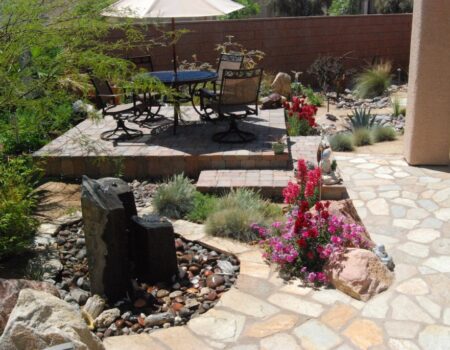 A patio with a table and chairs, water fountain and flowers.